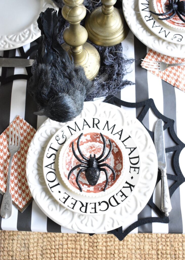 halloween placesetting with white plate orange transferware salad plate on black felt spider web place mat with orange white check paper napkin to left of plate black crow on table above plate