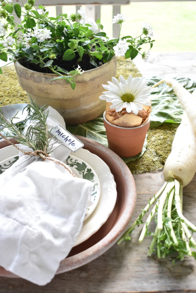 carrot muffin in terra cotta pot with shasta daisy stem in center sitting beside garden party theme place setting 