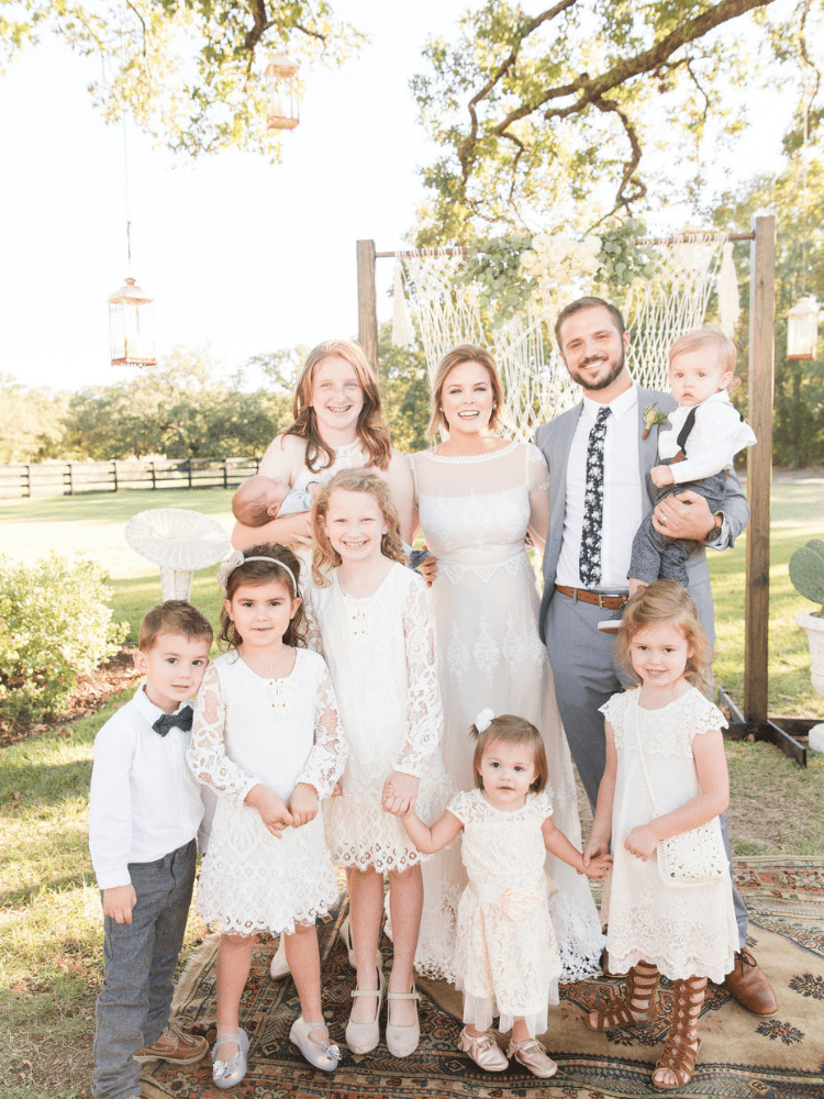 bride and groom standing in front of macrame wedding backdrop with children that were a part of the wedding