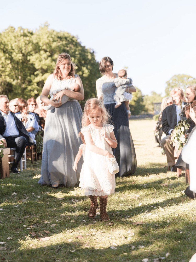 flower girsl walking down the aisle at an outdoor boho style wedding 