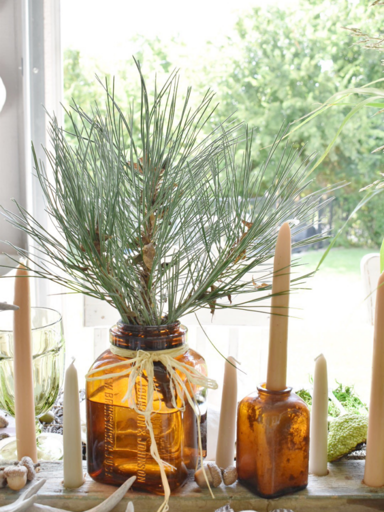 amber vase filled with pine branch and amber bottle with a taper sticking out for table centerpiece