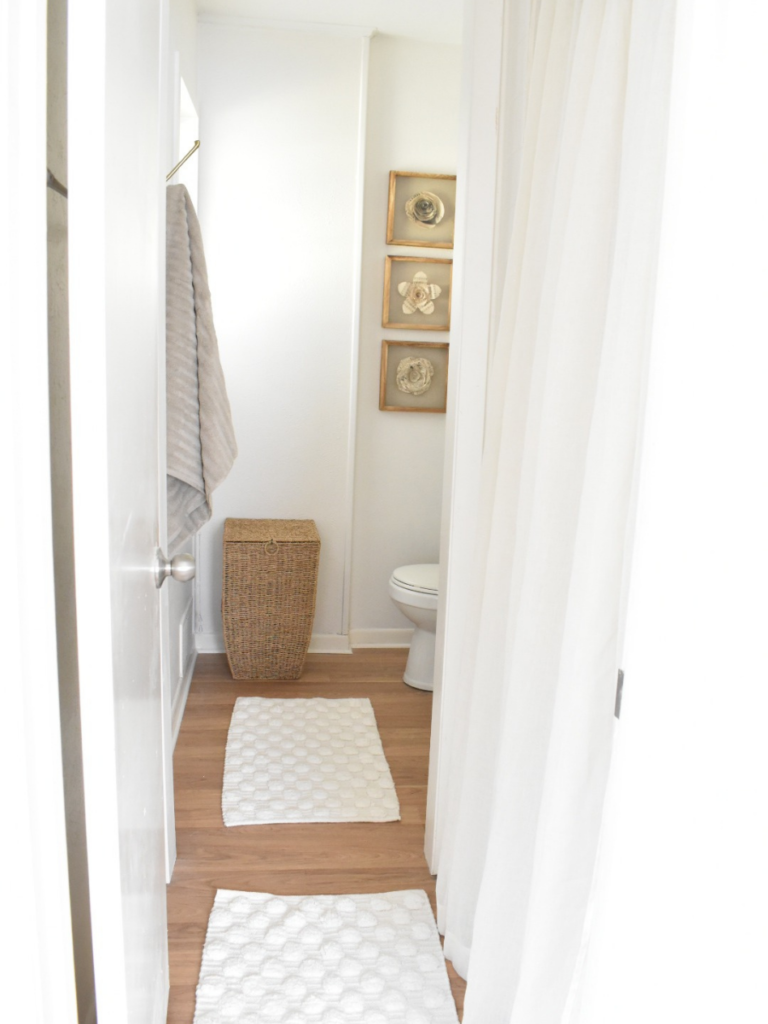 view into bathroom from bedroom light wood floors white rugs wicker hamper