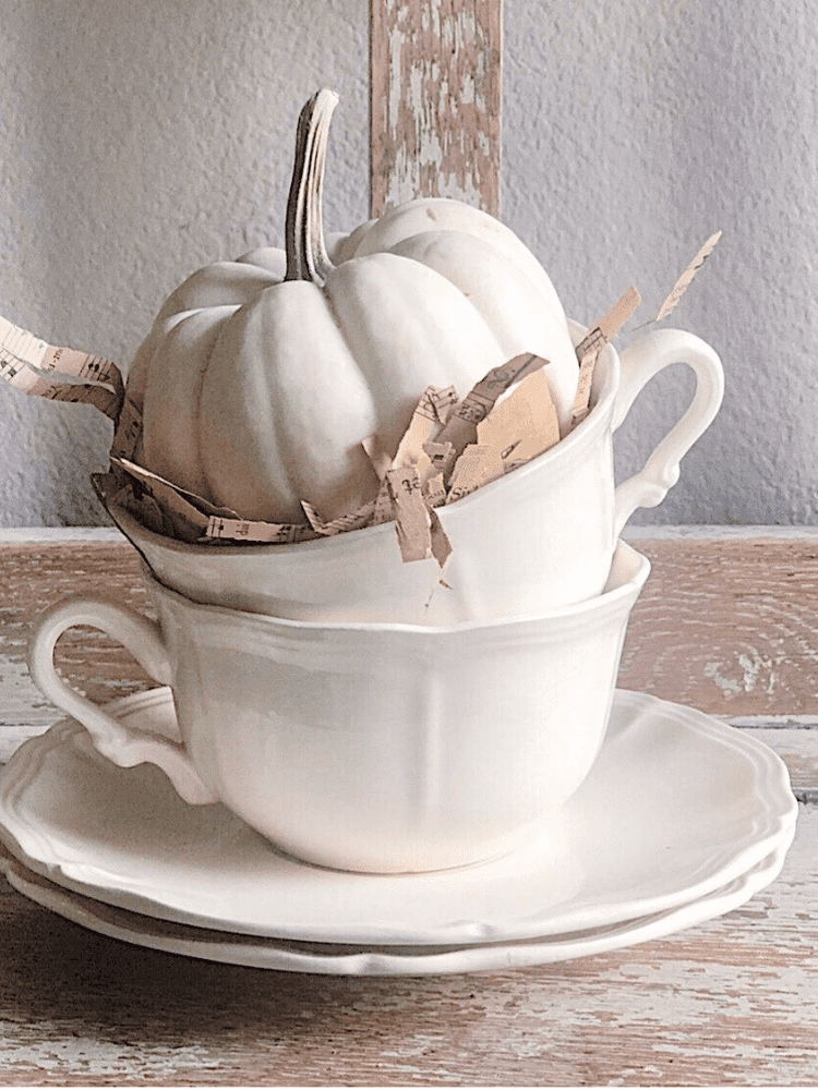 stack of white teacups on 2 saucers with a mini white pumpkin sitting in the top