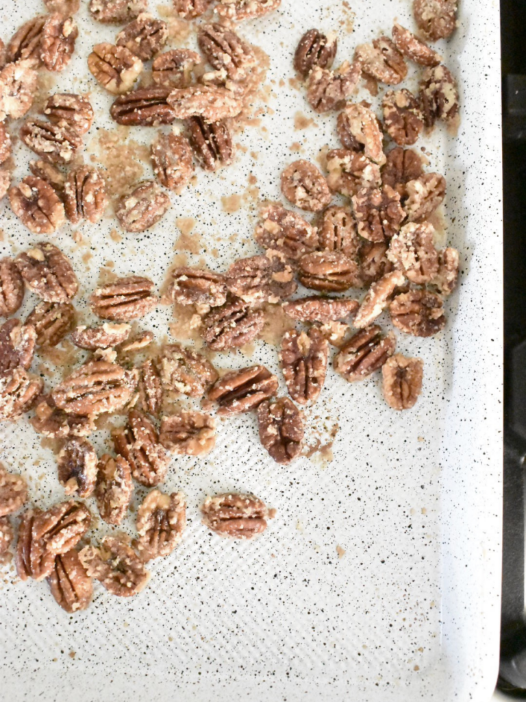 pecan halves coated in sugar laying on a white baking sheet