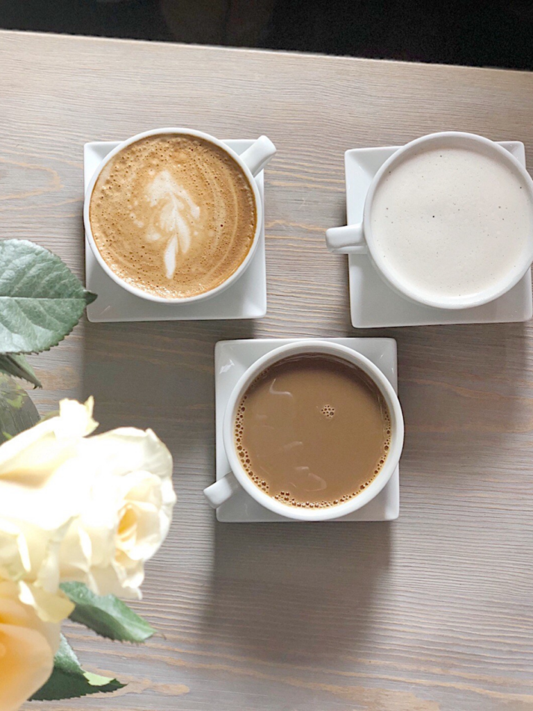 overhead shot of 3 cups coffee white mugs on white square saucers on light wood talbe yellow rose edgei n pic