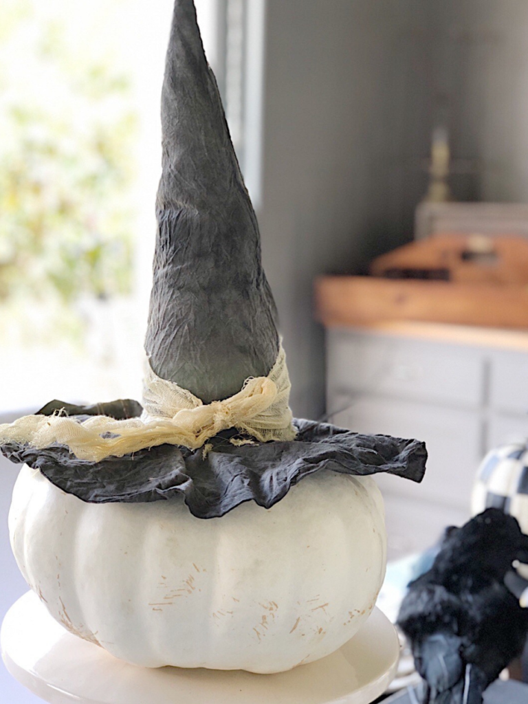 white heirloom pumpkin on white cake stand with witches hat on top 