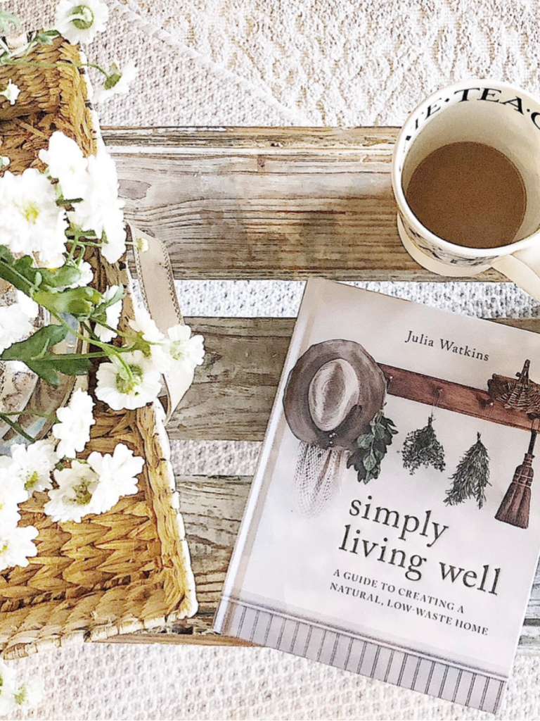 simply living well hardback book on top of vintage bench with cup of coffee and white flowers inside basket beside it