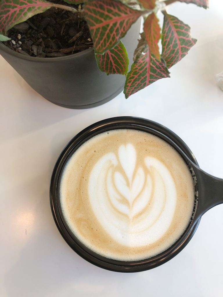 top view of latte with leaf design in black cup 