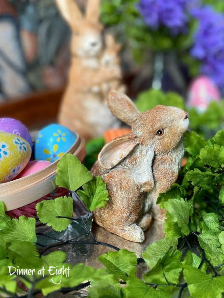 ceramic bunnies on tray with greenery beside easter eggs