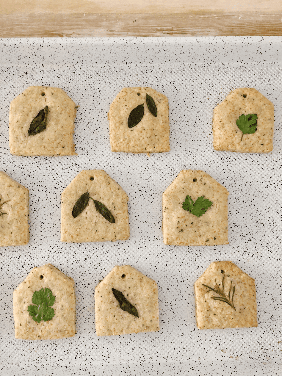 parmesan rosemary shortbread crackers cut into tea bag shape and fresh herb leaf on top of each cracker laying on white baking sheet