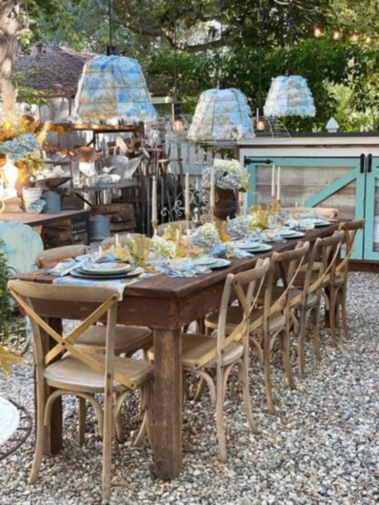 outdoor farm table with chairs around it set for a dinner party garden baskets made into lights hang over the table