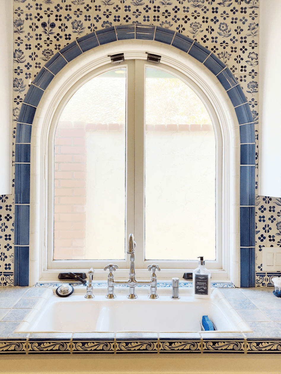 arched kitchen window over white sink with blue and white tile surround 