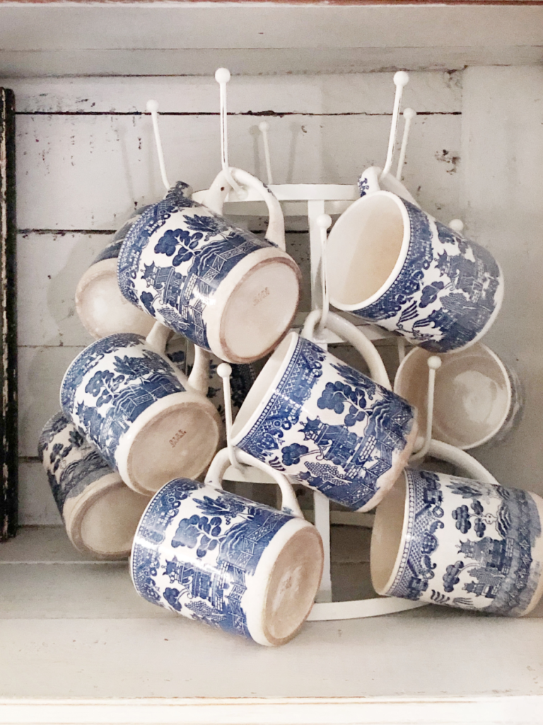 white mug tree with 8 blue transferware mugs inside white shelf