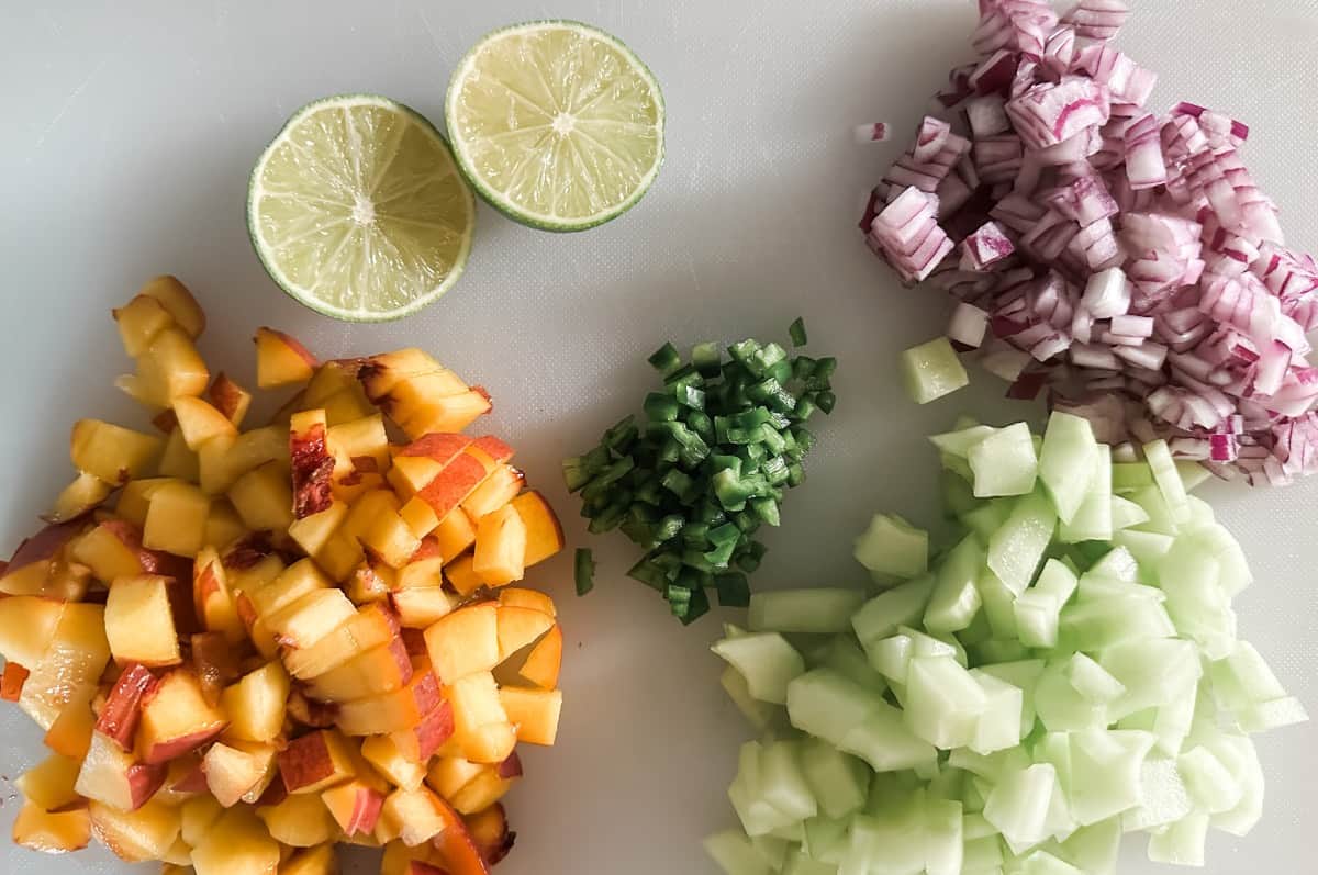 peach cucumber salsa ingredients on cutting board chopped peaches chopped cucumber chopped onion lime slices