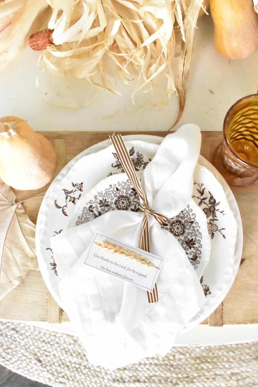 overhead view of thanksgiving place setting cutting board placemat brown transferware dinner plate stacked with salad plate white napkin tied with brown stripe ribbon on top of plate pear and gold goblet beside 