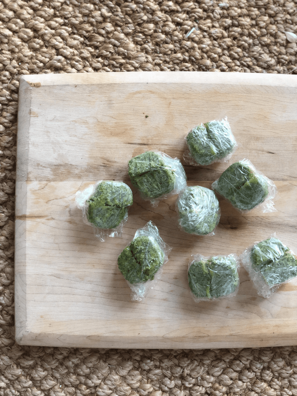 late summer harvest basil pesto frozen in ice cube trays and wrapped in saran wrap for freezing