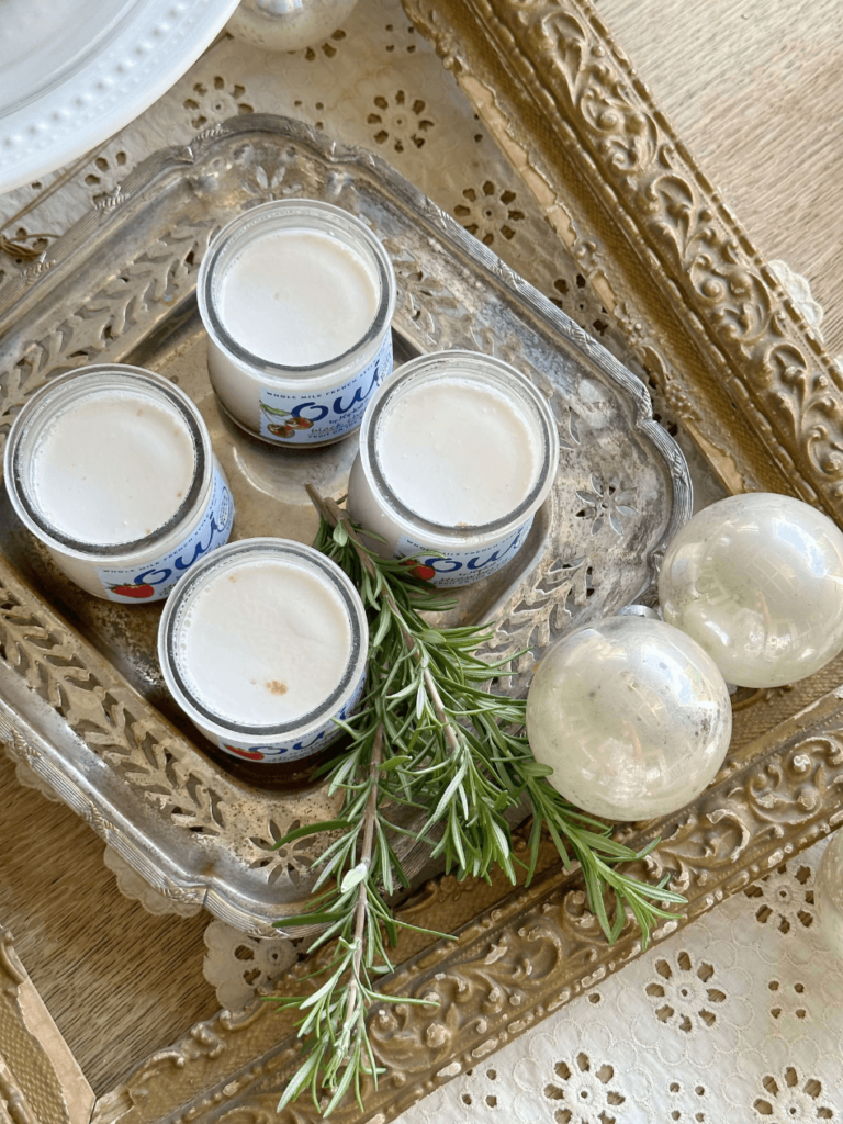 overhead view of 4 glass jars of yogurt on silver tray with sprigs of rosemary beside and silver vintage christmas balls beside