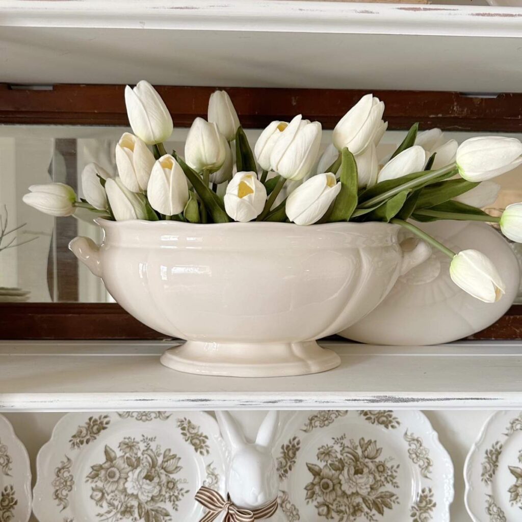 white faux tulips in white soup tureen inside china cabinet