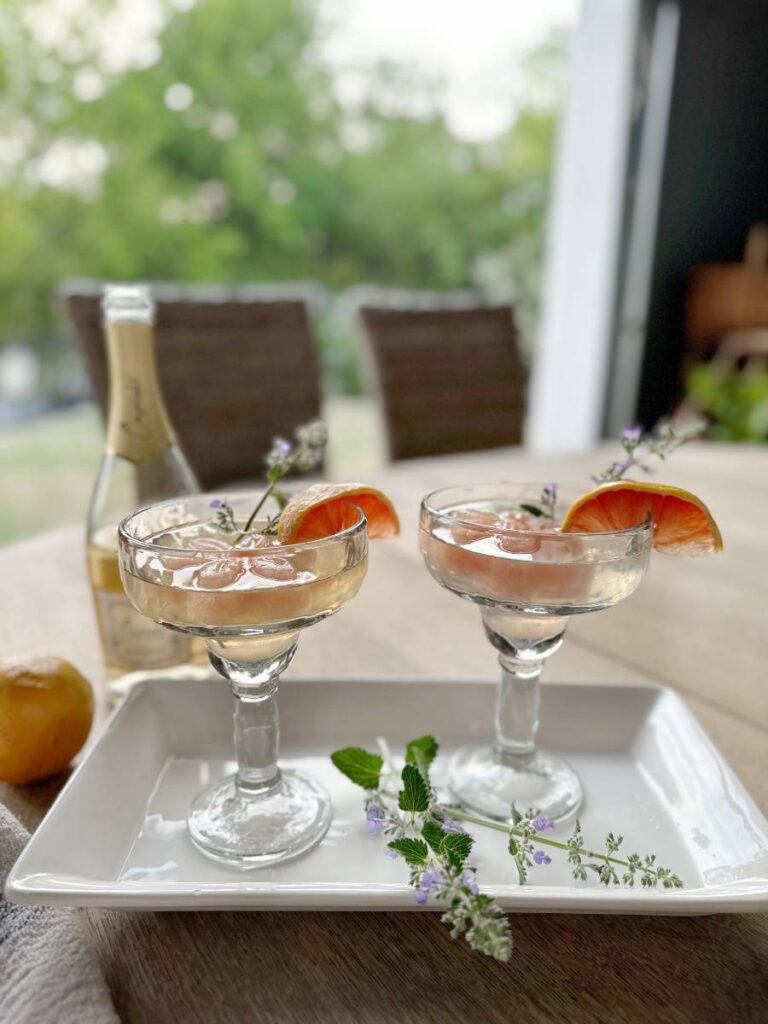 2 sparkling grapefruit cocktails with flower shape grapefruit ice cubes grapefruit slice on side of glass sitting on white tray