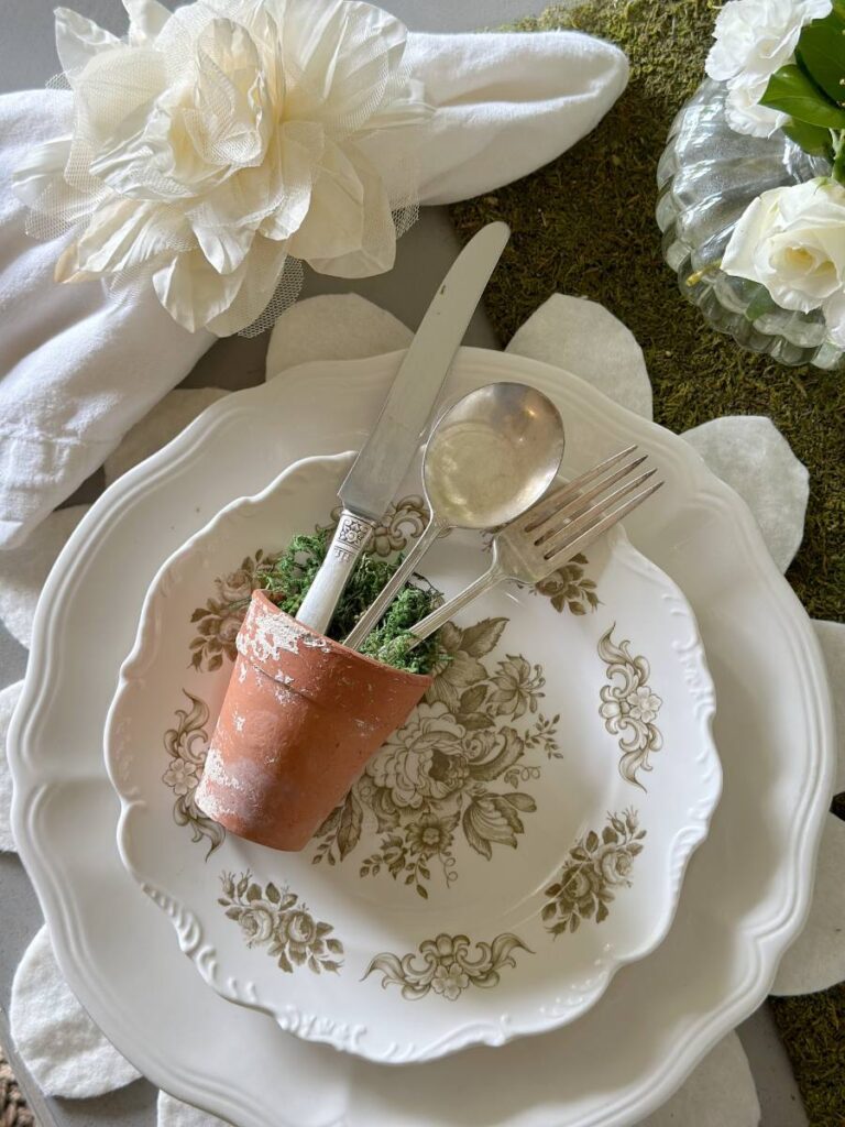 Floral Inspired Mother's Day place setting with white flower shape placemat white plates with silverware in small clay pot on top of plate