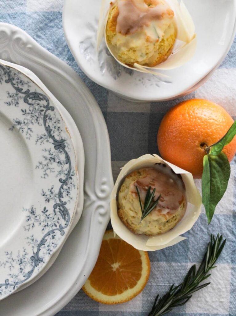 rosemary orange muffin with rosemary on top sitting beside orange and a blue and white plate