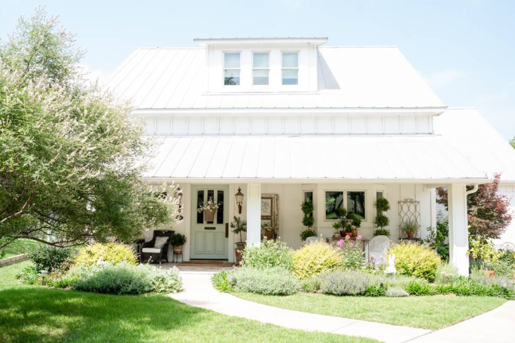 front of white farmhouse with cottage garden flower beds 