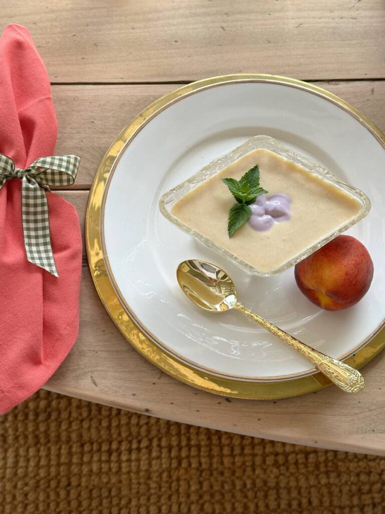 chilled peach soup in clear vintage bowl with mint leaf garnish on white plate