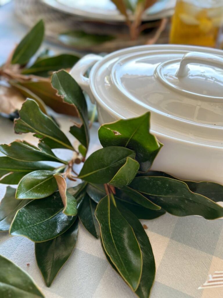 magnolia leaves beside white covered dish for dinner table set up