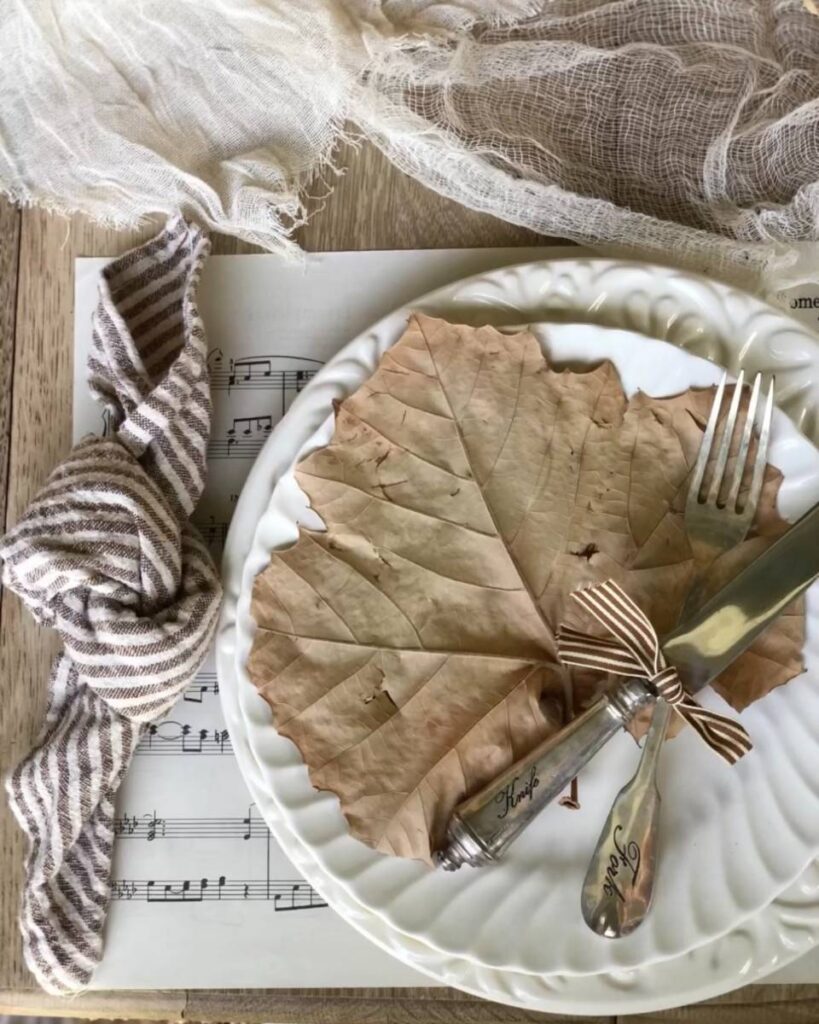 place setting with large dried leaf on white plate brown stripe napkin