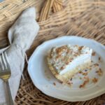 slice of coconut cream pie with toasted coconut on white plate sitting on wicker basket tray