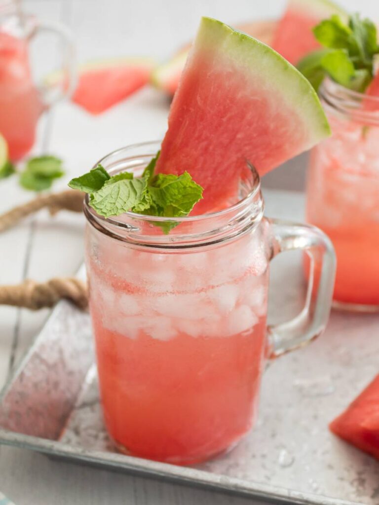 mason jar with handle with pink watermelon cocktail mint sprig and watermelon slice garnish