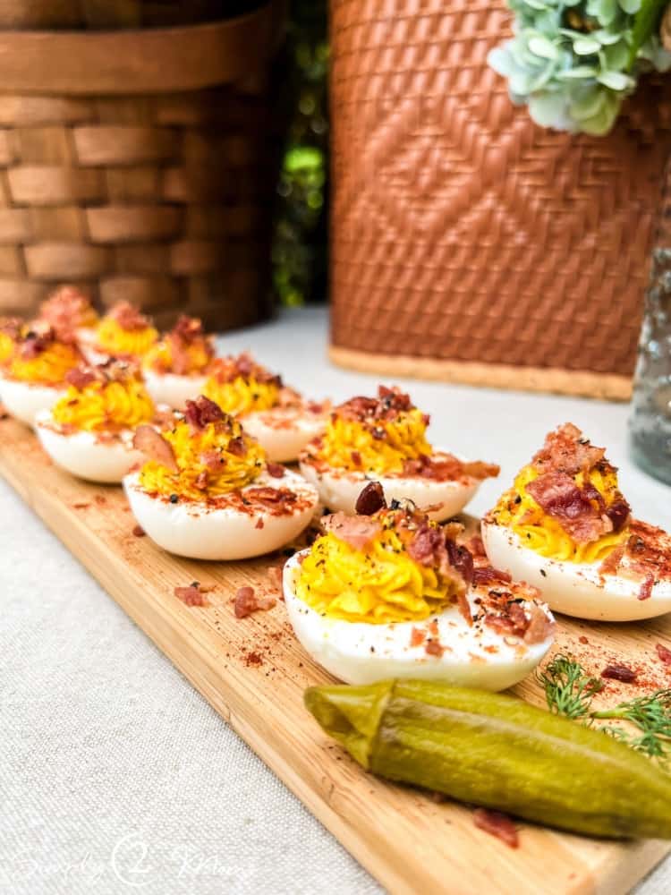 wooden board with deviled eggs topped with bacon