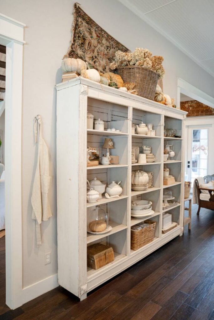 white kitchen hutch with  fall decor pumpkins and dried hydrangeas on top white dishes inside