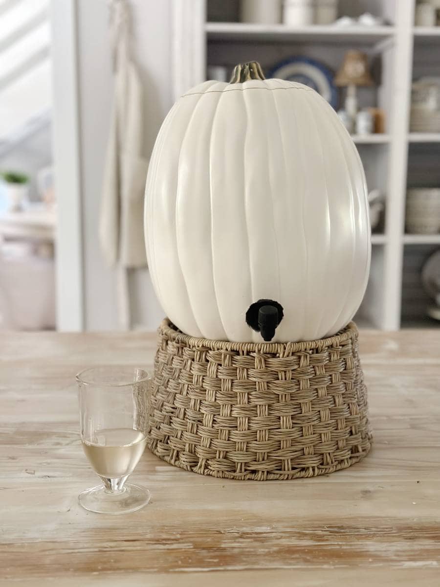 white faux pumpkin with wine bag with spigot inside standing on woven beverage stand