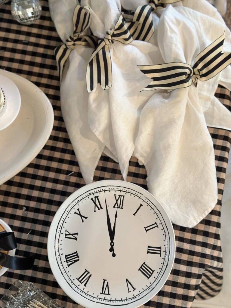 white clock plates stack of white napkins with black striped ribbon tied sitting an black check tablecloth on table