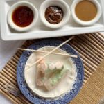 white plate with 3 Asian spring rolls and chopsticks beside tray of 3 bowls of dipping sauces