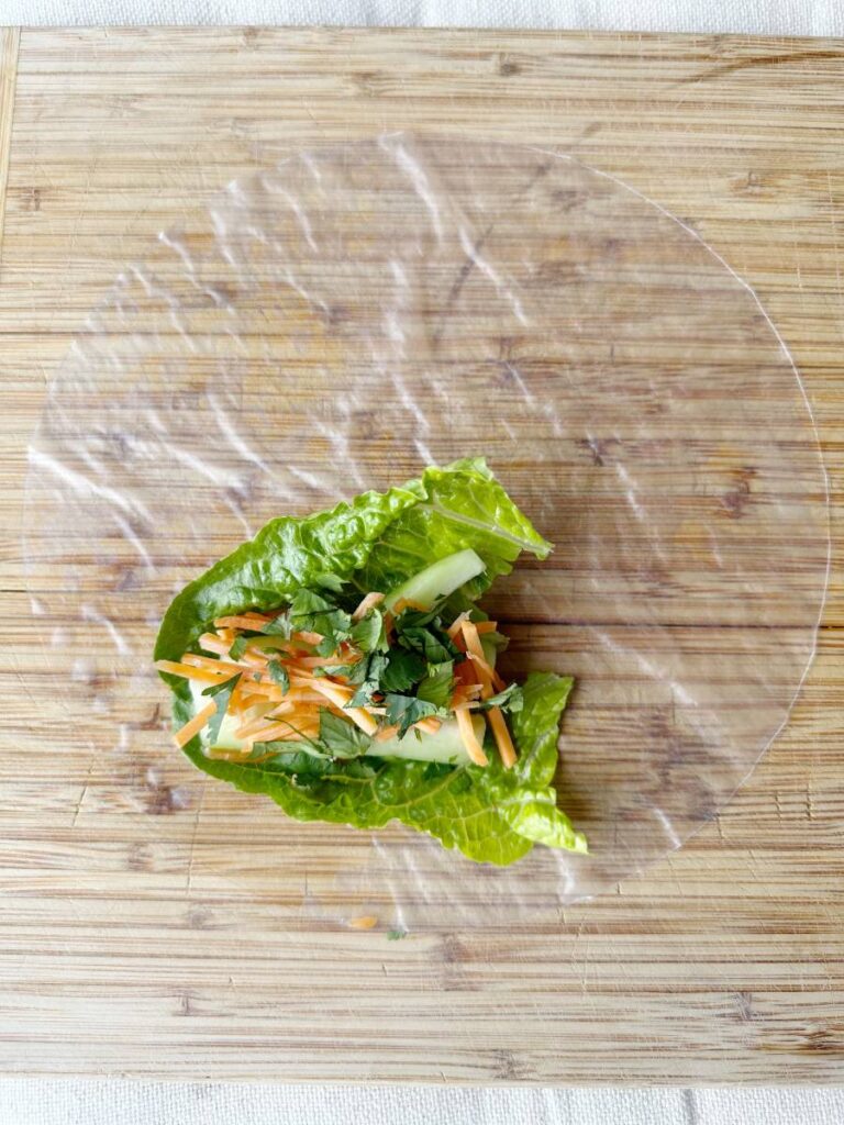 lettuce leaf cucumber slices carrot slices and cilantro on rice paper wrapper for spring roll