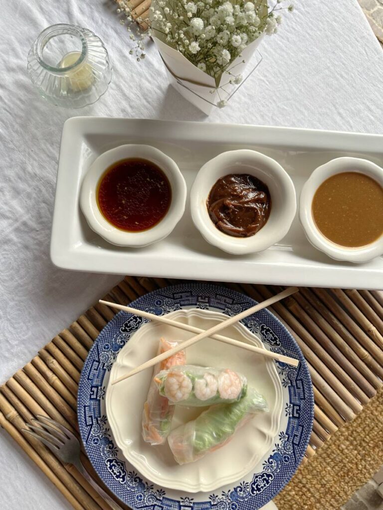 white plate with 3 Asian spring rolls and chopsticks beside tray of 3 bowls of dipping sauces