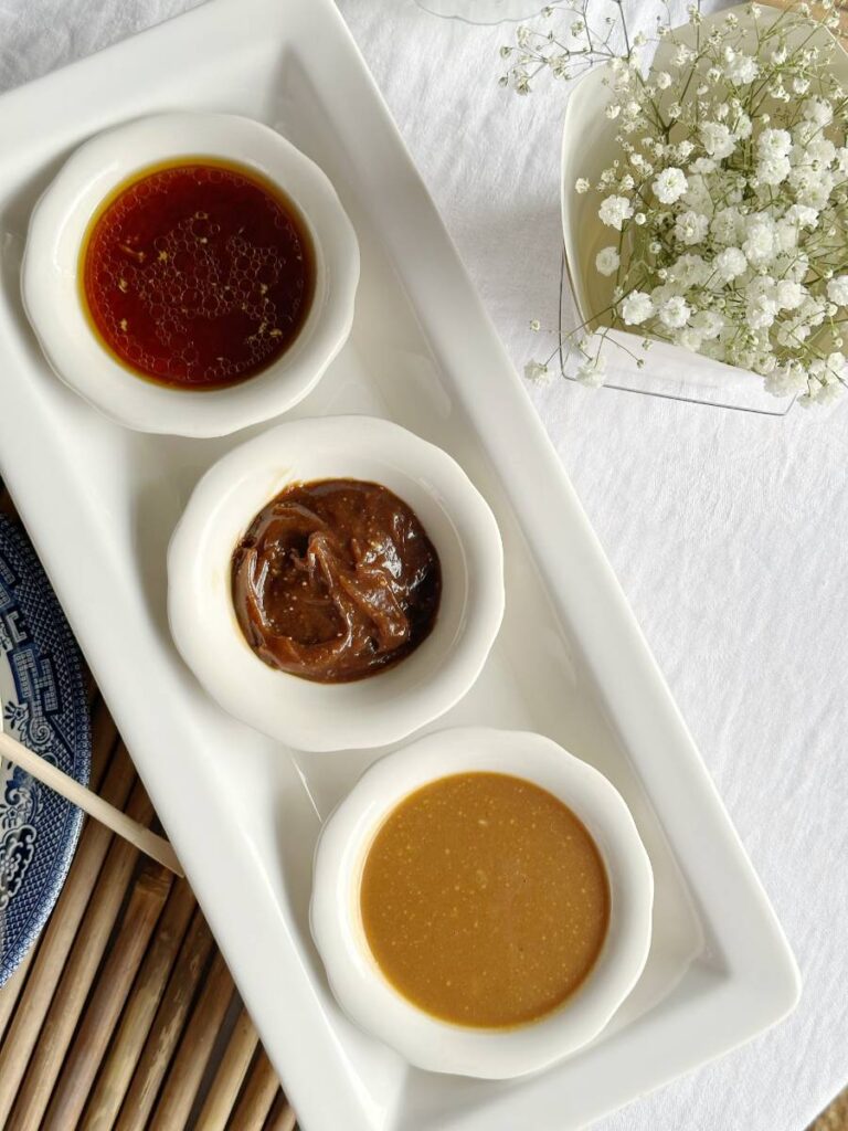 3 small white bowls of dipping sauces for Asian spring rolls on white tray. Peanut Hoisin dipping sauce