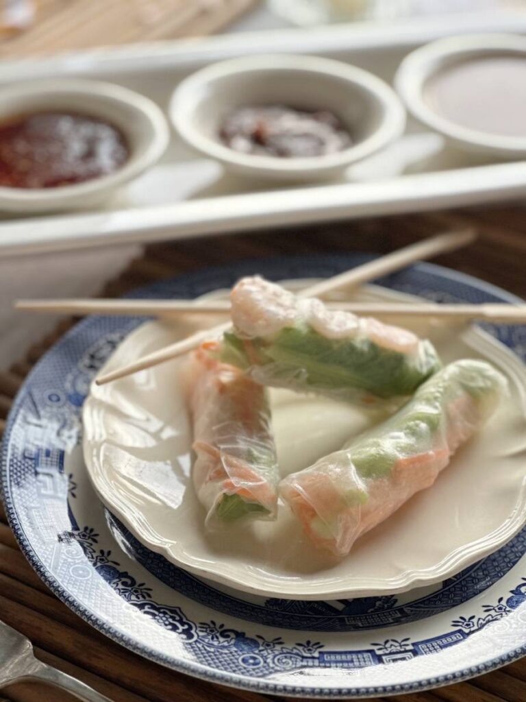 white plate with 3 Asian spring rolls and chopsticks beside tray of 3 bowls of dipping sauces