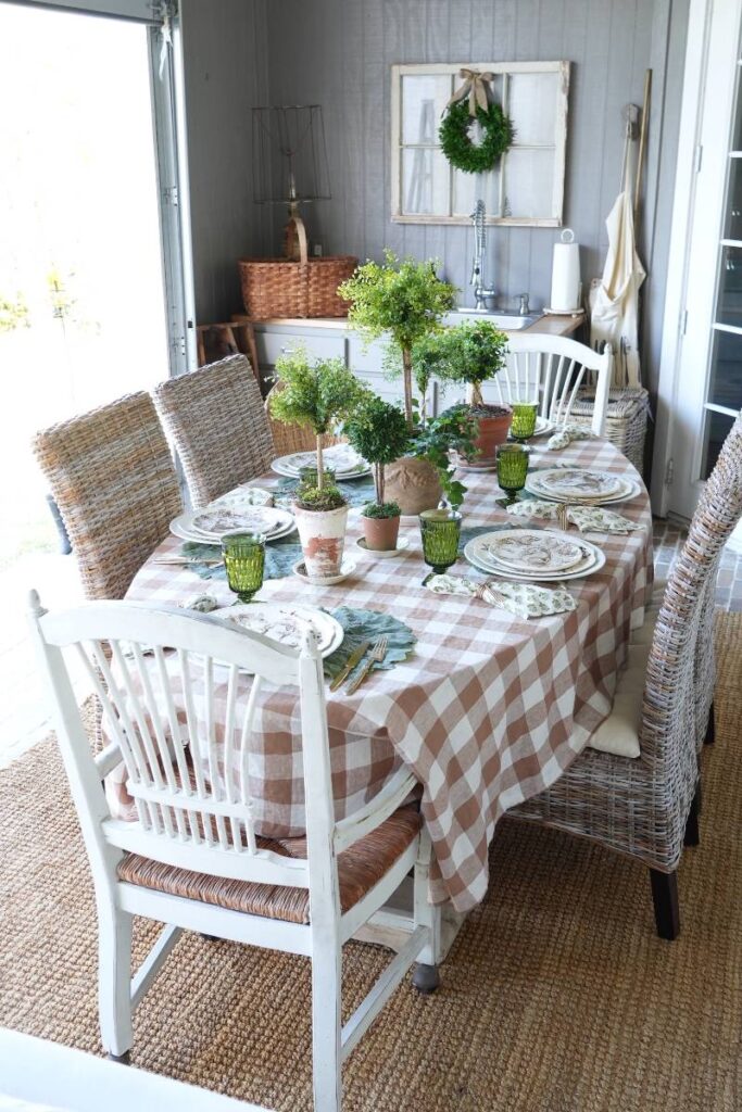 brown check tablecloth with brown pattern bunny plate green block print napkin gold flatware on cabbage leaf placemat at 6 place settings for spring table topiaries down center of table