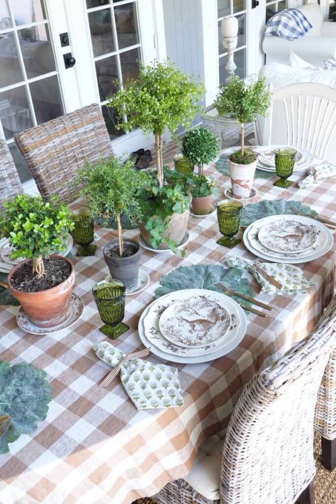 brown check tablecloth with brown pattern bunny plate green block print napkin gold flatware on cabbage leaf placemat at 6 place settings for spring table topiaries down center of table