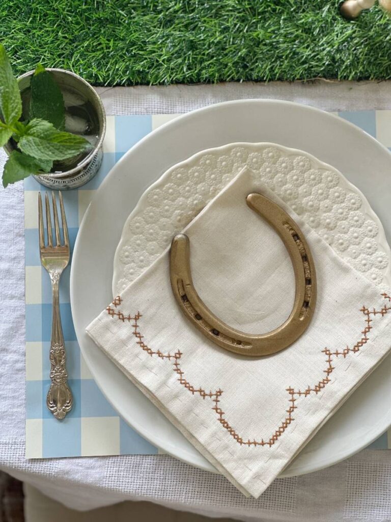 white dinner plate stacked with white salad plate folded napkin on top and gold horseshoe mint julep cup beside plate for Kentucky Derby place setting