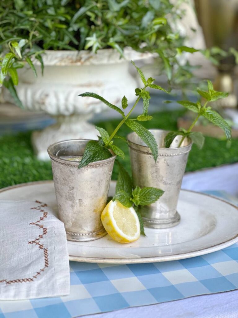 2 traditional mint julep cocktails with a lemonade twist in silver julep cup with mint sprig garnish on white platter with lemon slice and mint sprig