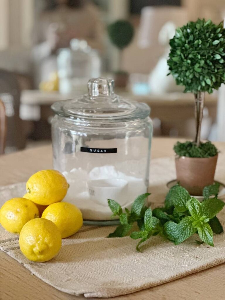 glass cannister of sugar lemons and mint piled beside and faux topiary