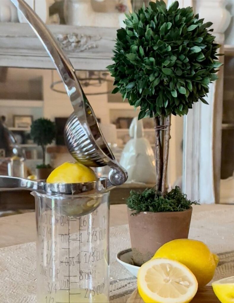 lemon in lemon squeezer on top of measuring cup whole lemons beside it