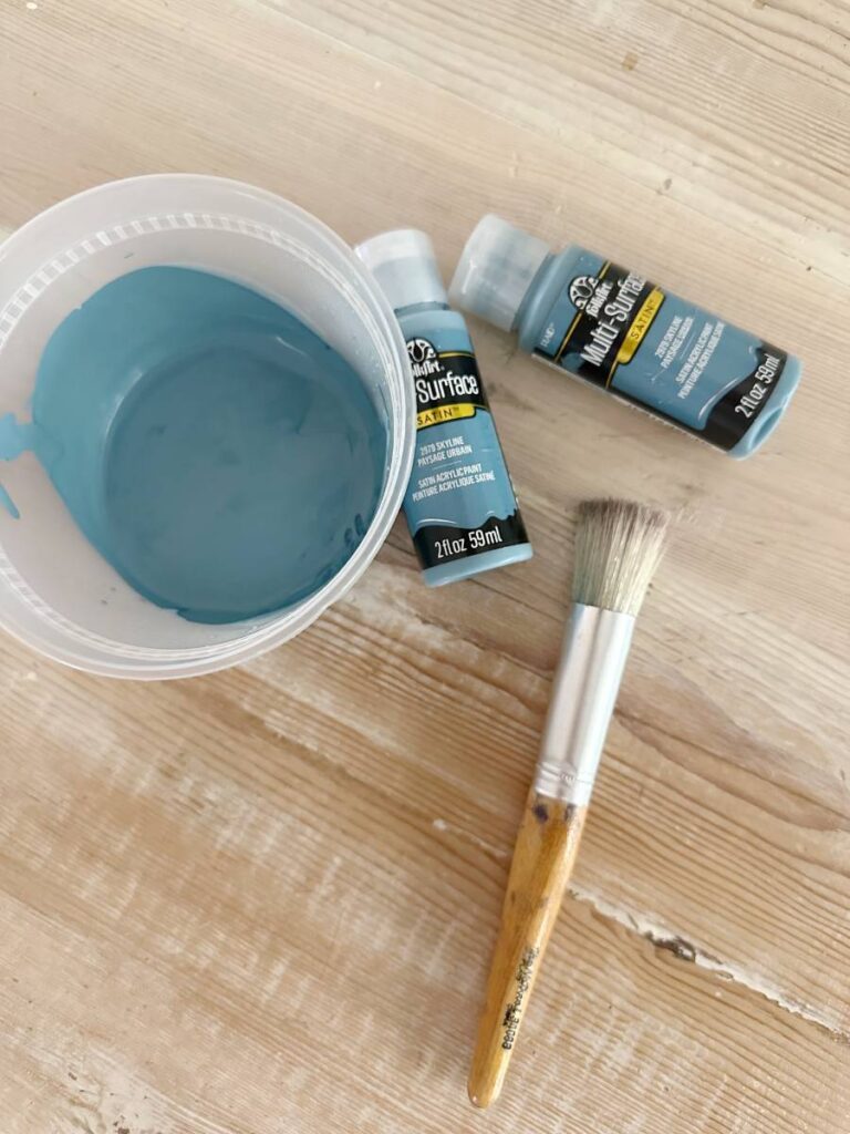 container of blue paint stencil brush and 2 bottles of blue craft paint