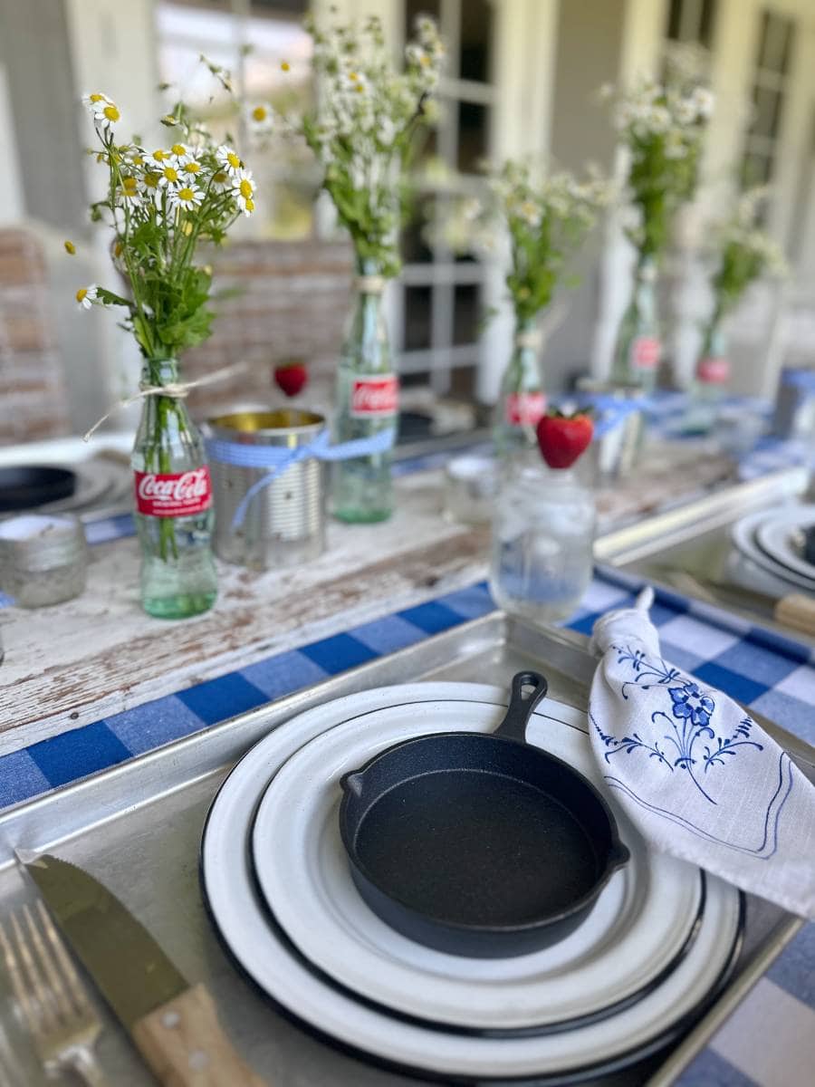 cookie sheet for placemat white with black trim enamelware salad and dinner plate stacked with mini cast iron skillet on top white napkin with blue floral print beside plate