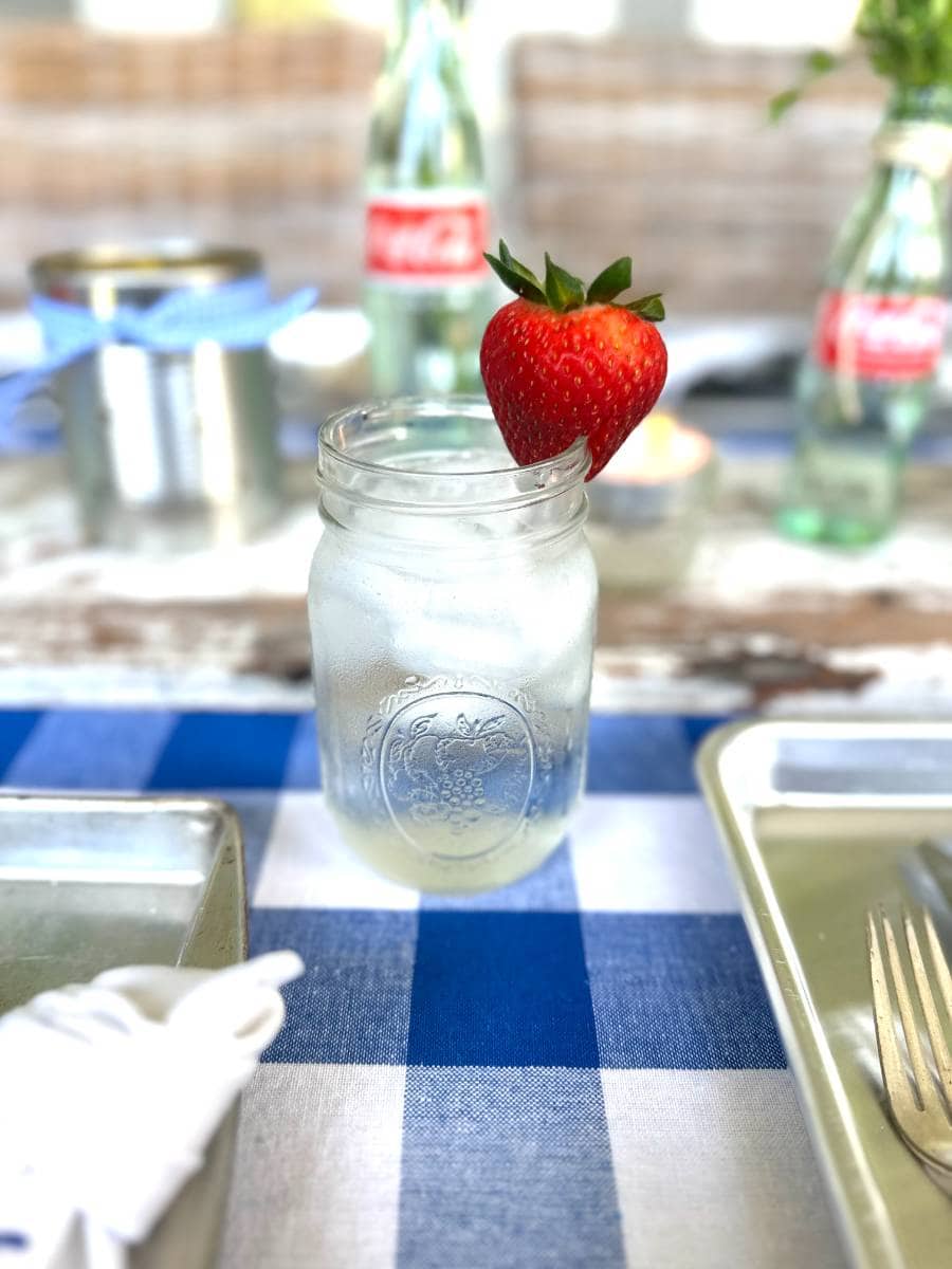 mason jar with ice water and strawberry garnish on side of glass