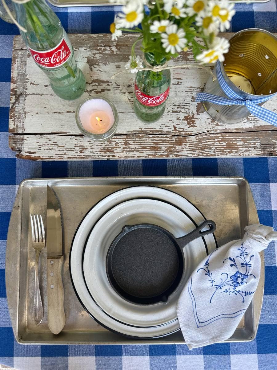 cookie sheet for placemat white with black trim enamelware salad and dinner plate stacked with mini cast iron skillet on top white napkin with blue floral print beside plate